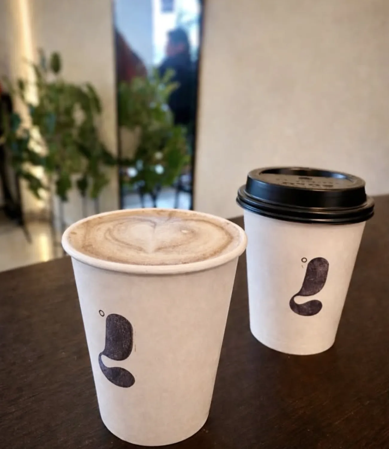 Dos vasos de Lattitude Coffee sobre una mesa, un latte con arte de corazón junto a un vaso para llevar