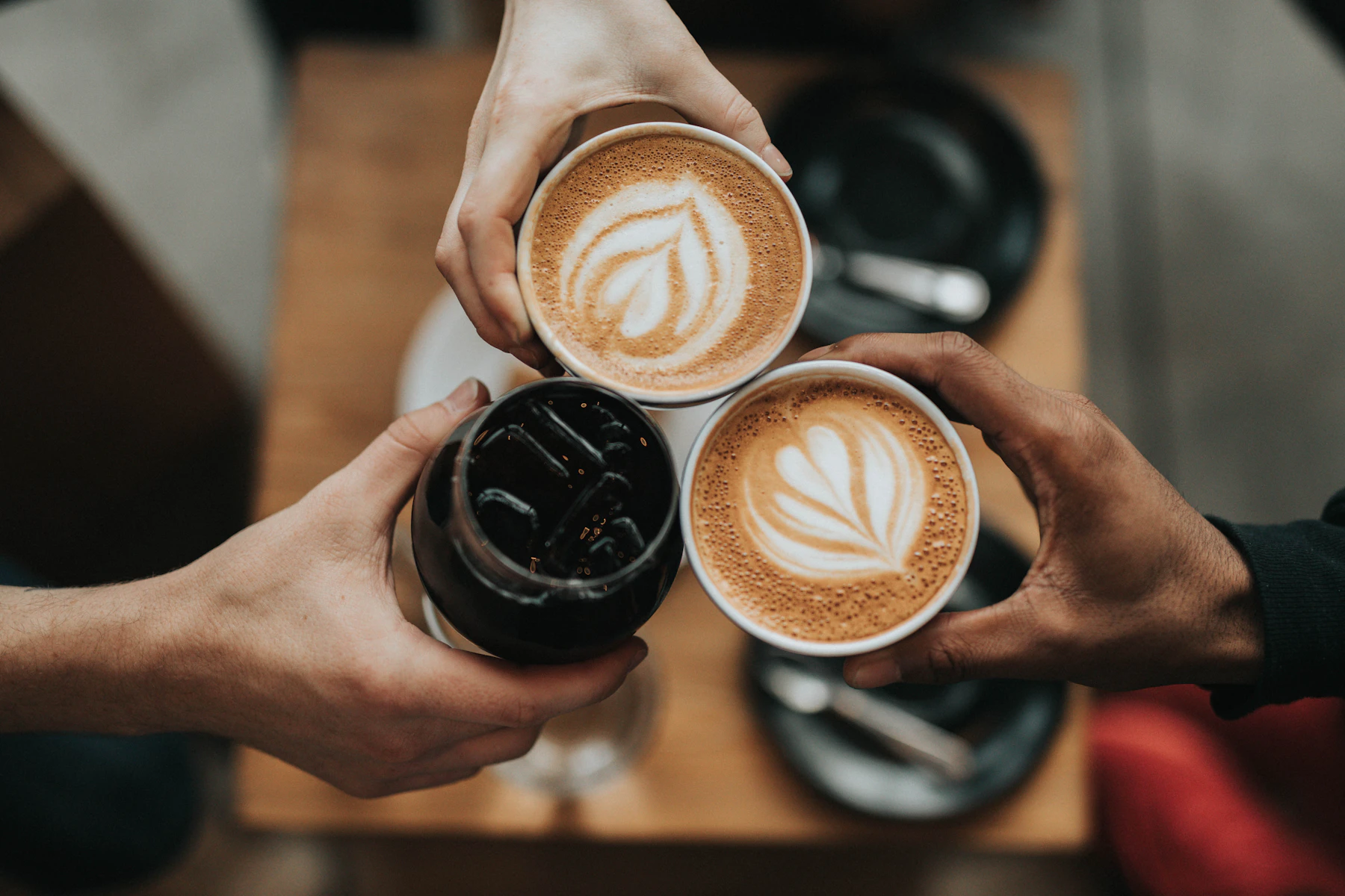 Tres personas brindando con flat whites de arte latte y un cold brew en Lattitude Coffee